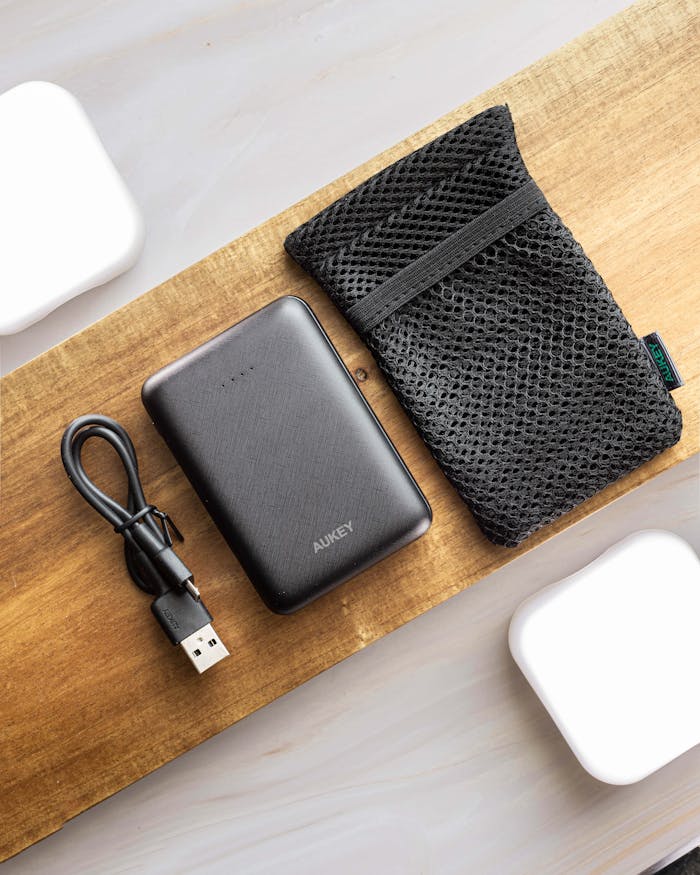 Home Flat lay of a black power bank with a USB cable and mesh pouch on wood.